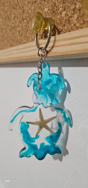 Llavero de Tortuga, de color transparente y color azul con una estrella de mar en su interior acompañado de una pequeña tortuga en tono azul claro.